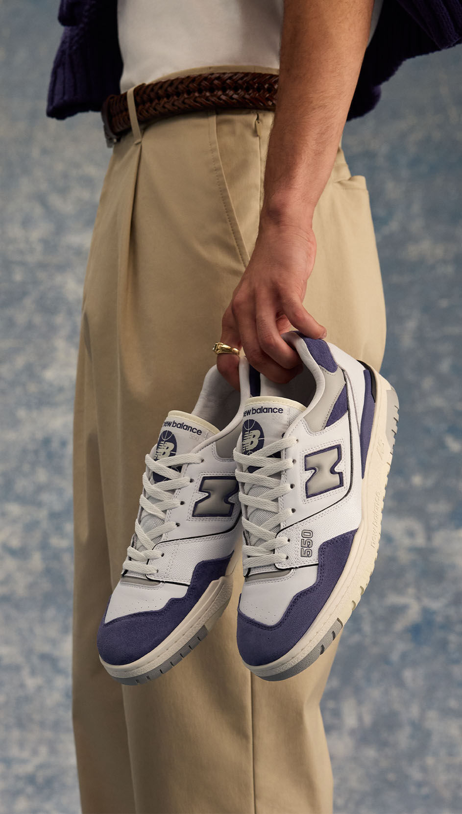 Model, dressed stylishly, holding New Balance 550 sneakers. 